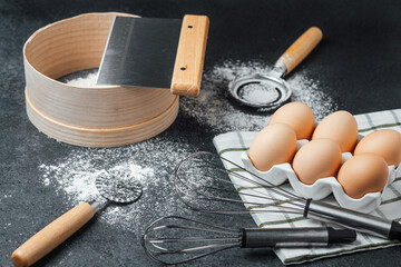 Baking essentials with fresh eggs and kitchen tools on dark background