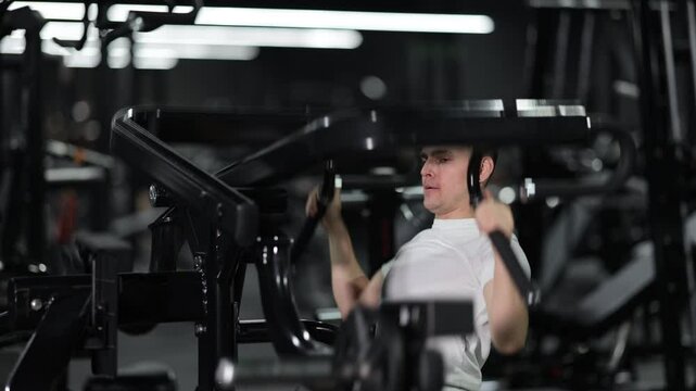 Focused young man training on plate-loaded lat pulldown machine at gym, building back and arm strength as part of healthy and active lifestyle trend. High quality 4k footage