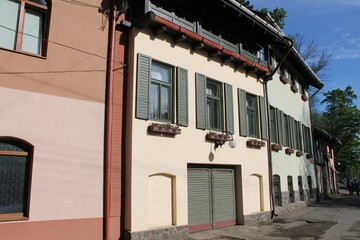 Charming two-story building with historic architecture and green shutters in a sunny neighborhood, showcasing vibrant flower boxes along the windows