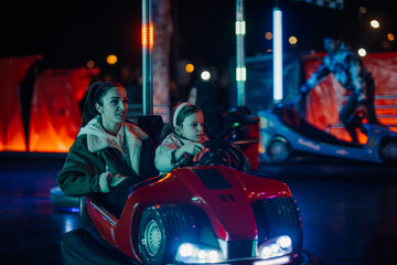 Mother and daughter enjoying bumper cars at amusement park night ride