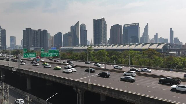 Many cars moving along the elevated Sirat expressway in Bangkok. Makkasan railway station and skyscrapers in the background in the day time