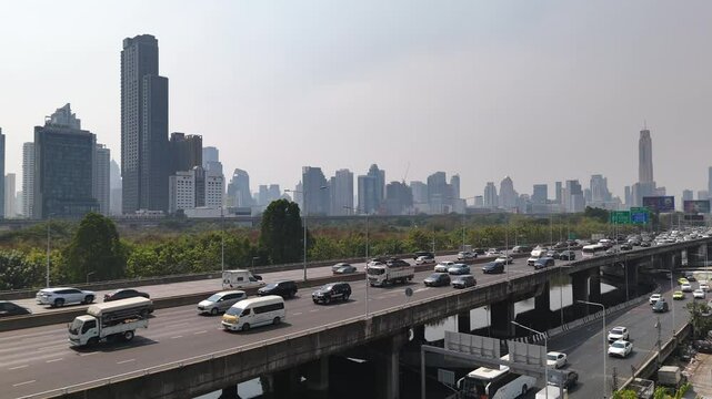 Busy Sirat expressway and elevated roads in Bangkok. Dense skyline of modern skyscrapers and office buildings in the background captured during a hazy daytime.
