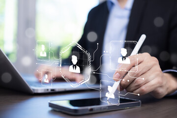 A businessman uses a digital pen on a smartphone, selecting a virtual user profile icon, symbolizing online networking, HR technology, and digital recruitment. AI-powered hiring solutions.