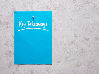The word key takeaways on a blue sheet of paper pinned to a white concrete wall.
