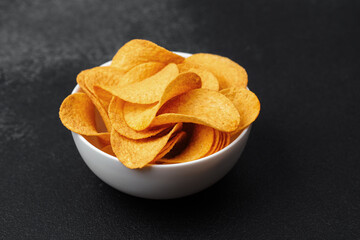 Bowl of crispy potato chips on a dark surface ready for snacking
