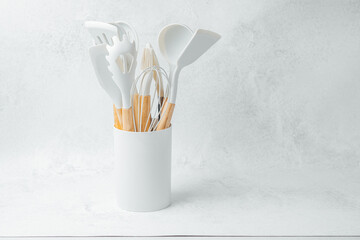 Kitchen utensils arranged in a white container on a light surface