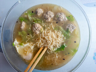 A bowl of home made instant noodles soup with pork meat balls, poached eggs, Chinese leaf and hot chilli oil.