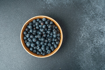 Fresh blueberries in a ceramic bowl placed on a dark surface