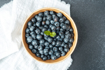 Fresh blueberries in a wooden bowl on a textured gray surface