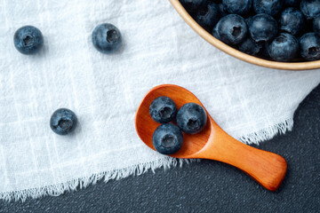 Fresh blueberries in a wooden spoon beside a bowl on a linen cloth