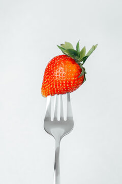 Strawberry balanced on a fork against a light background in a simple setting