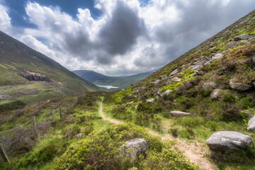 Stunning Silent Valley Reservoir path that is surrounded by vibrant, lush foliage of Mourn Mountains and dramatic clouds, perfect for nature lovers, photographers, and avid hikers, Northern Ireland