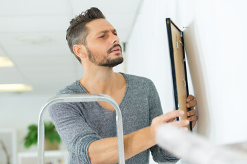 male carpenter hanging picture frame on wall at home