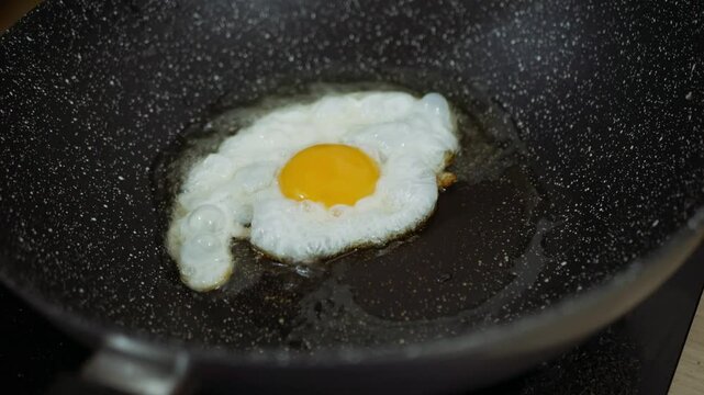 Cooking fried eggs sunny side up with a sizzling oil in frying pan.