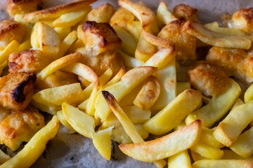 Golden crispy fries and golden batter fish freshly served on a cooking tray, showcasing a...