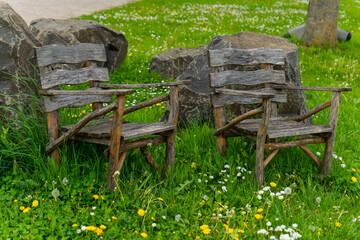 Old wooden chairs nestled in a vibrant green field surrounded by colorful flowers against a...