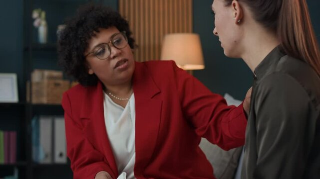 Medium shot of female African American psychologist listening to female Caucasian patient explaining her problems during therapy session