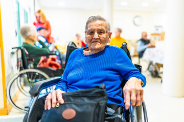 Elderly woman sitting in wheelchair in nursing home with other seniors in background