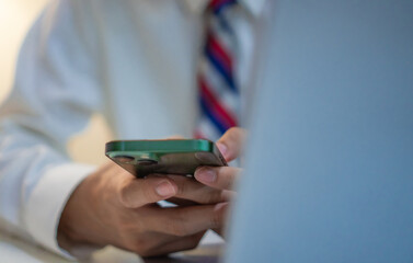 Close up hand of business man using smartphone and computer laptop working in office. Young professional male employee sitting on table, chatting and texting for business   in corporate workplace