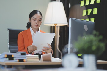 Young adorable Asian businesswoman working with work document during the night, working overtime at...