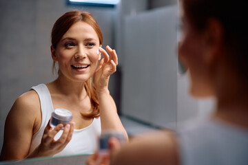 Happy woman applying face cream during her daily skincare routine.