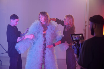 Full length shot of production assistants adjusting costume on actress during shoot while director filming scene on camera