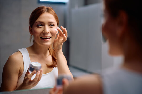 Happy woman applying face cream during her daily skincare routine.