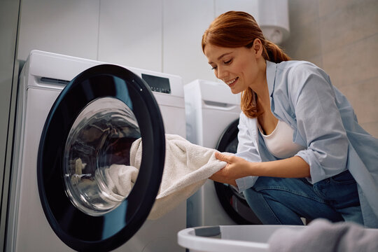 Happy woman using washing machine in laundry room.