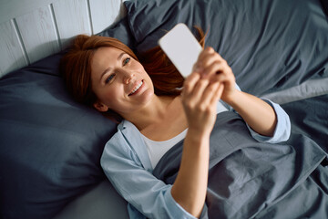 Above view of happy woman using mobile phone in bed.