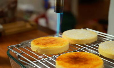Close-up view of caramelizing crème brûlée with a kitchen torch, golden crisp sugar crust forming, homemade dessert preparation.