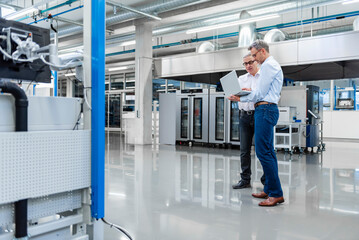 Two professionals discussing with a laptop in a modern production hall