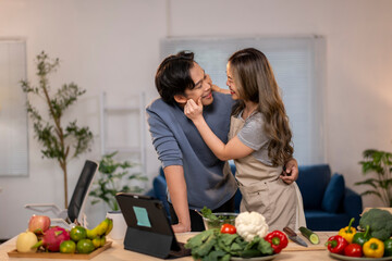 A man and woman are hugging in a kitchen with a laptop on the table