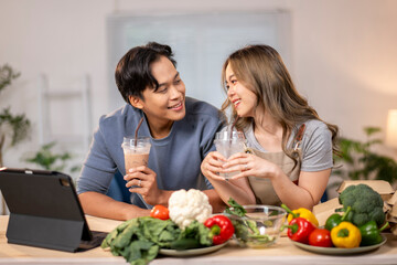 A man and a woman are sitting at a table with a laptop and a bowl of vegetables