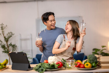 A man and woman are standing in a kitchen, holding drinks and laughing