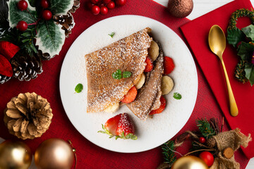 Chocolate crepes filled with strawberry and fresh banana. Top view table with christmas decorations.