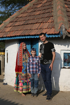 Tourist family: woman in traditional national Indian costume, Meghwal folk dress and man, child. Village, India. Indian local people. Tribal native woman, Meghwal tribe in Gujarat. Bride, house, home