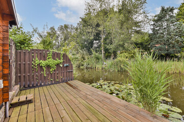 A serene garden scene featuring lush greenery surrounding a tranquil pond, wooden deck, and a rustic wooden gate, inviting a peaceful atmosphere.