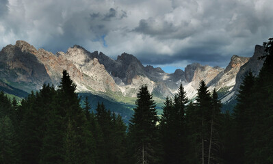 Landscape in the Alps mountain tops in the background, 
mountain sticking out of a forest in the italian alps 