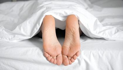 Healthy looking feet under a blanket sleeping in a bed with white sheets