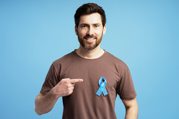 Man pointing at blue ribbon supporting prostate cancer awareness on blue background