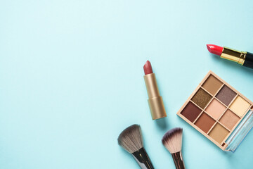Beauty products on blue background. Cosmetic palette, brushes and lipsticks. Top view.