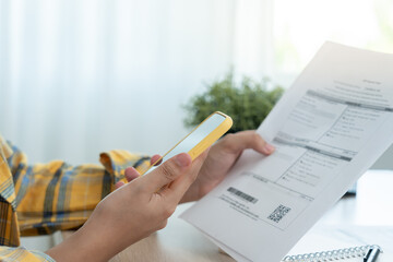 woman use phone scan barcode or QR codes to pay credit card bill after receiving document invoice. payment, receive, paying electricity, digital payments, technology, scanning, financial transactions