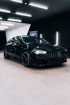 Front-side view of black Mercedes Benz CLA 45 S AMG C118 in detailing studio. Aggressive design, red brake calipers, and LED headlights under modern lighting. Marketing materials, advert or press.