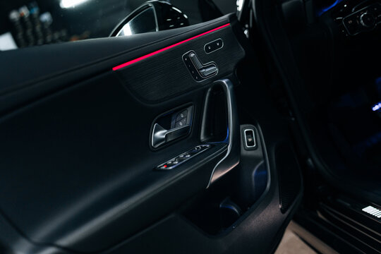 Close-up of Mercedes-Benz CLA 45 S AMG driver door with red ambient lighting &ndash; premium black interior, chrome accents, seat adjustment controls and stitching details for luxury automotive presentation