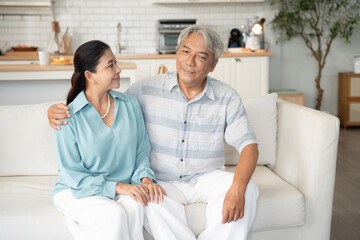 Asian senior man embracing wife on sofa and talking together. Retired couple spending time in the morning at home. Healthy and life insurance concept