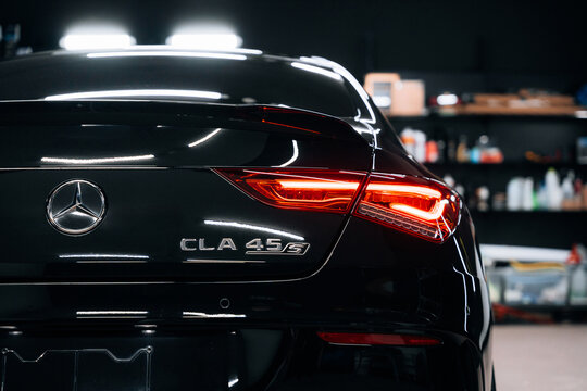 Medium shot of Mercedes Benz AMG C118 rear with illuminated taillight and CLA 45S badge &ndash; sleek black paint and performance design in moody garage lighting. Promo, advert marketing materials.