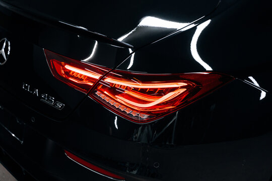 Medium shot of Mercedes Benz AMG C118 rear with illuminated taillight and CLA 45S badge &ndash; sleek black paint and performance design in moody garage lighting. Promo, advert marketing materials.