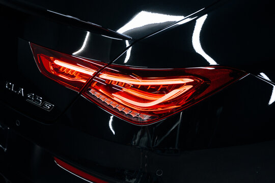 Medium shot of Mercedes Benz AMG C118 rear with illuminated taillight and CLA 45S badge &ndash; sleek black paint and performance design in moody garage lighting. Promo, advert marketing materials.