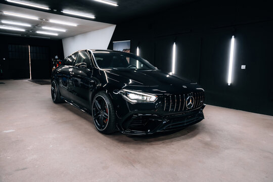 Front-side view of black Mercedes Benz CLA 45 S AMG C118 in detailing studio. Aggressive design, red brake calipers, and LED headlights under modern lighting. Marketing materials, advert or press.