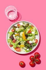 Vegetable salad with lettuce, vegetables, olives and feta cheese on bright pink background